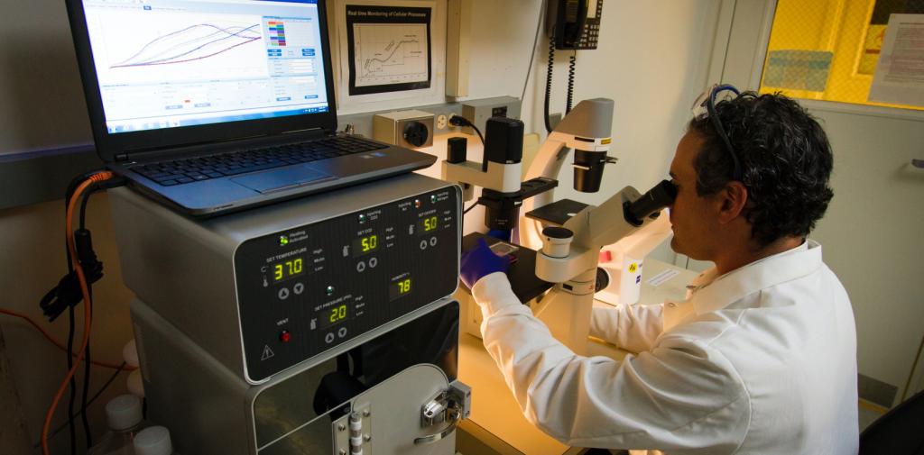 scientist looking in microscope next to large equipment