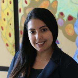 Maria Coronel, PhD smiling in a navy blazer in front of colorful background
