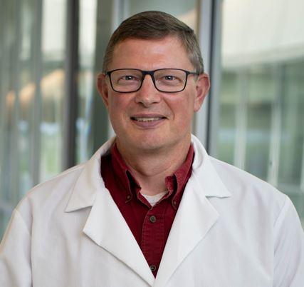 Headshot of Dr. Myers, smiling in white lab coat standing in front of windows