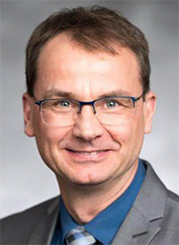 Headshot of Dr. Kretzler in gray blazer with blue shirt and eyeglasses