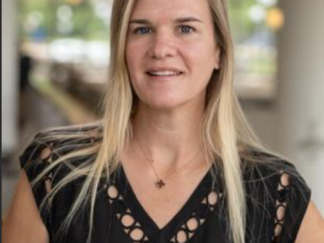 Headshot of Dr. Gallagher in black top standing in what appears to be a hospital corridor or room