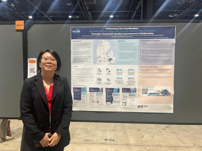 Dr. Lynn Ang dressed in black with red top, standing next to her poster at the event