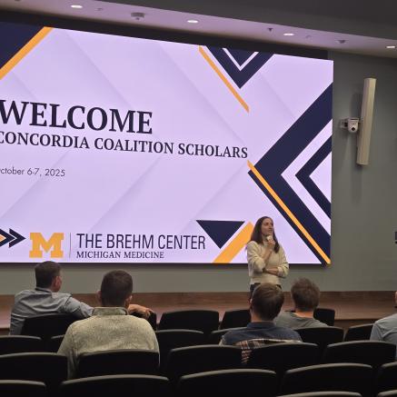 Dr. Hepler standing in front of large white screen, facing an audience 