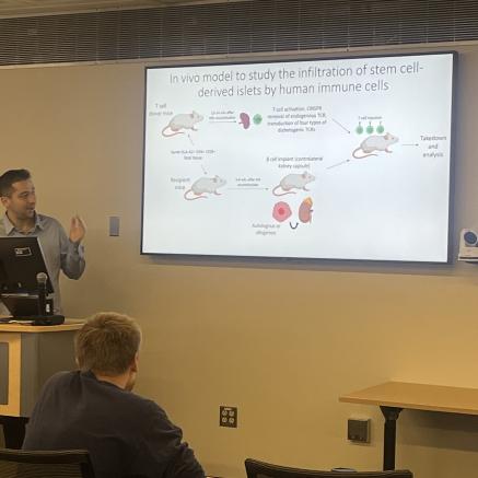Male standing behind podium sharing information on large white screen beside him