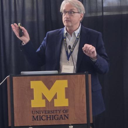 Dr. Clay Semekovich speaking behind a podium displaying the University of Michigan logo
